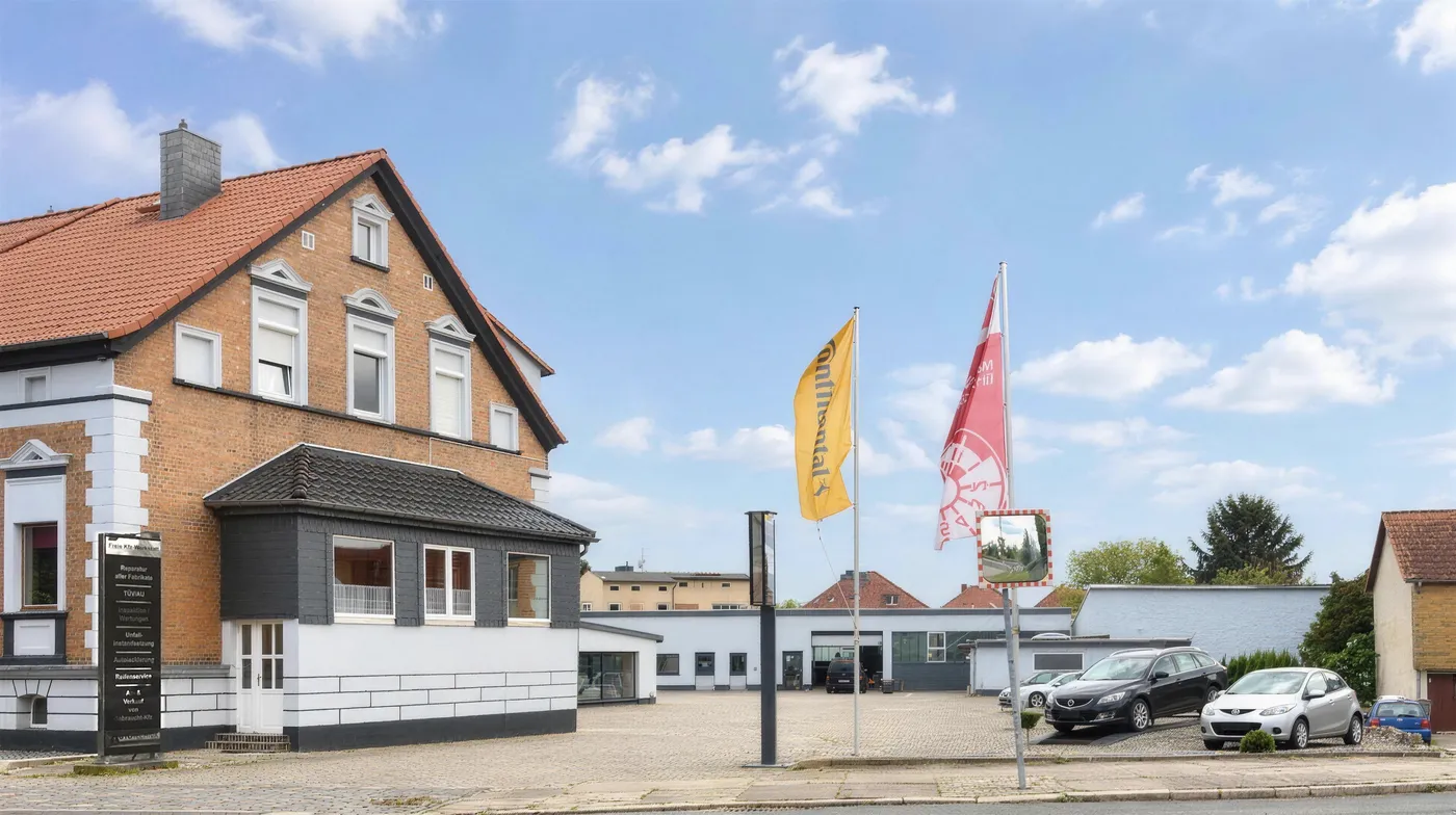 Die Werkstatt AUTOTECHNIK Kratzat von außen: Wohnhaus mit Werkstatthalle und Fahnen an der Hornhäuser Straße